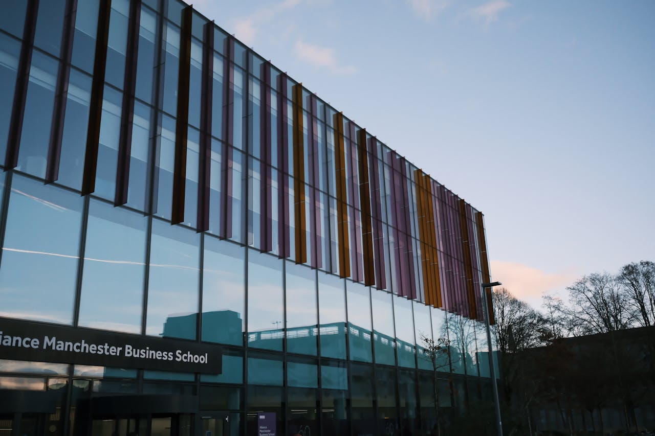 Modern architecture of Alliance Manchester Business School reflecting in glass facade at dusk.